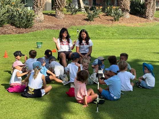 Two coaches leading a circle of young players in a lesson on the grass