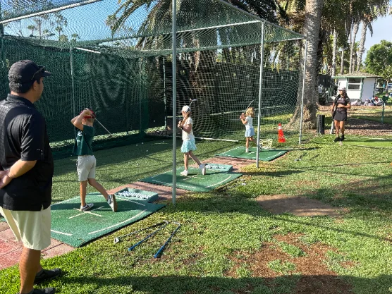 Players practicing full swings at the driving range with a coach watching