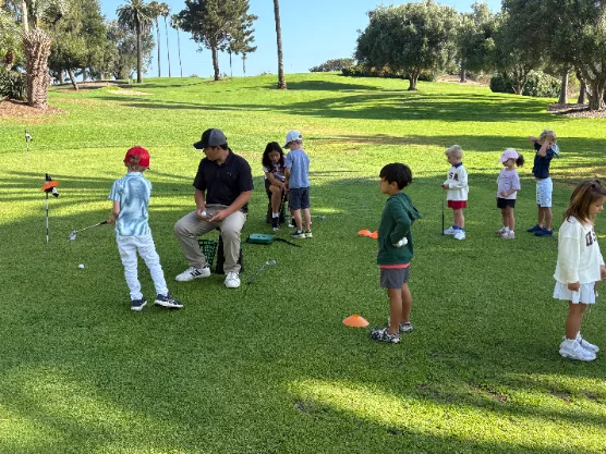 A coach leading a group golf clinic with several young players